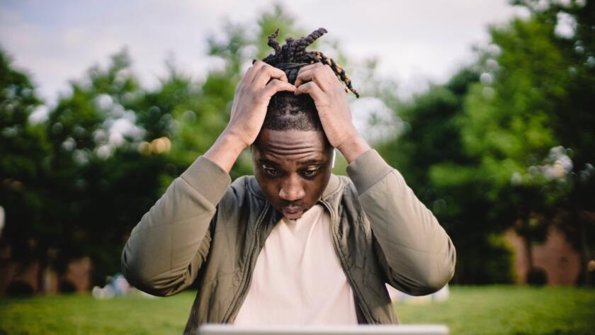 stressed black male entrepreneur working on laptop in park