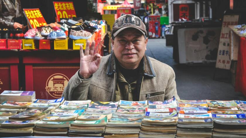 man in brown coat in front of books